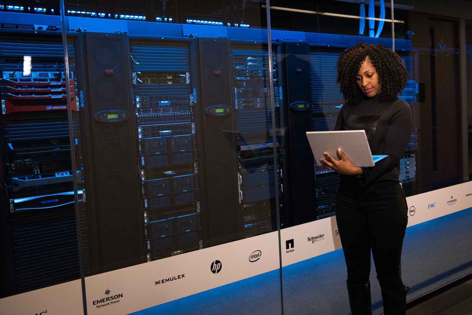 An engineer with a tablet walking a blue-lit data-centre aisle between server racks