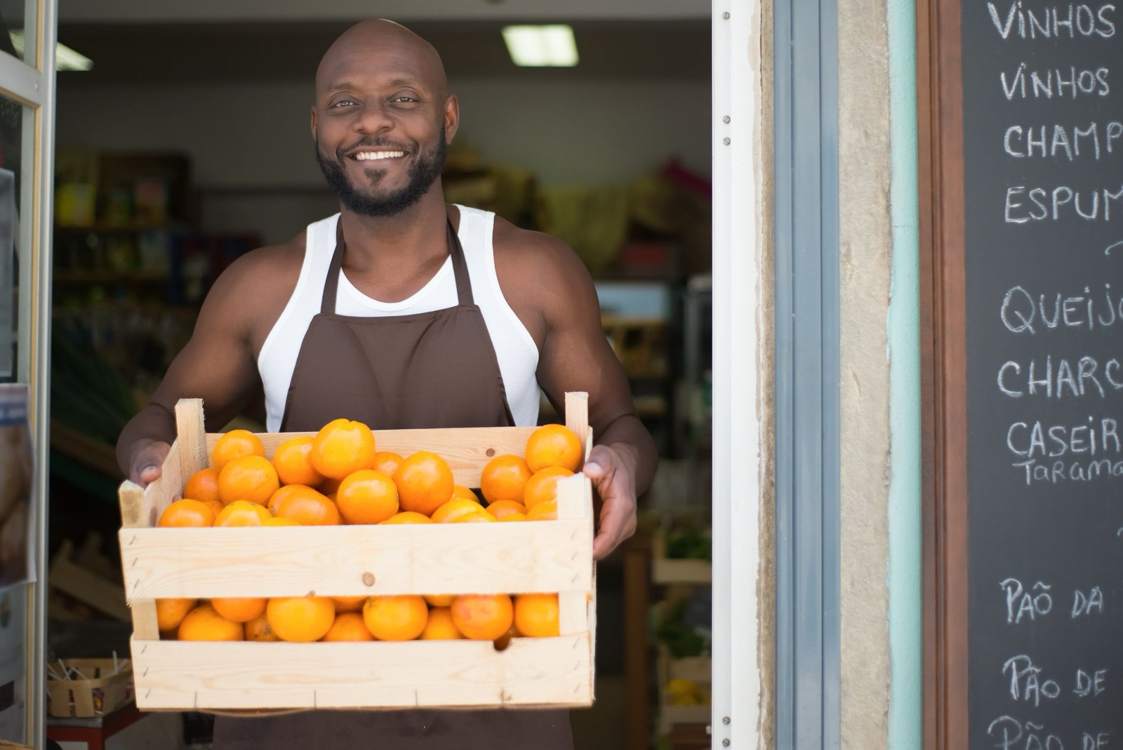 A shop owner in his doorway holding out a crate of fresh oranges