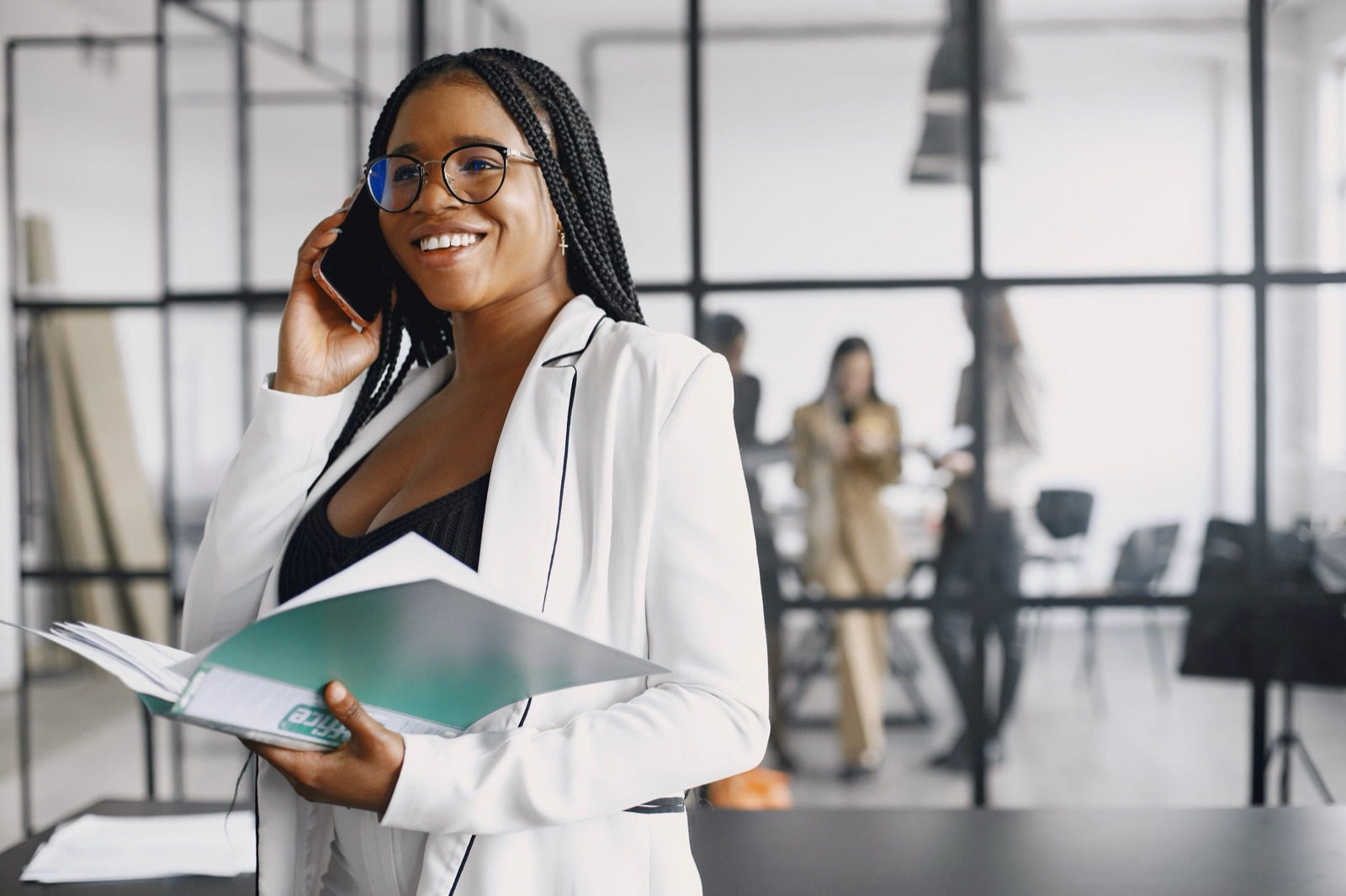 A professional smiling mid-conversation on a phone call, notes open in front of her