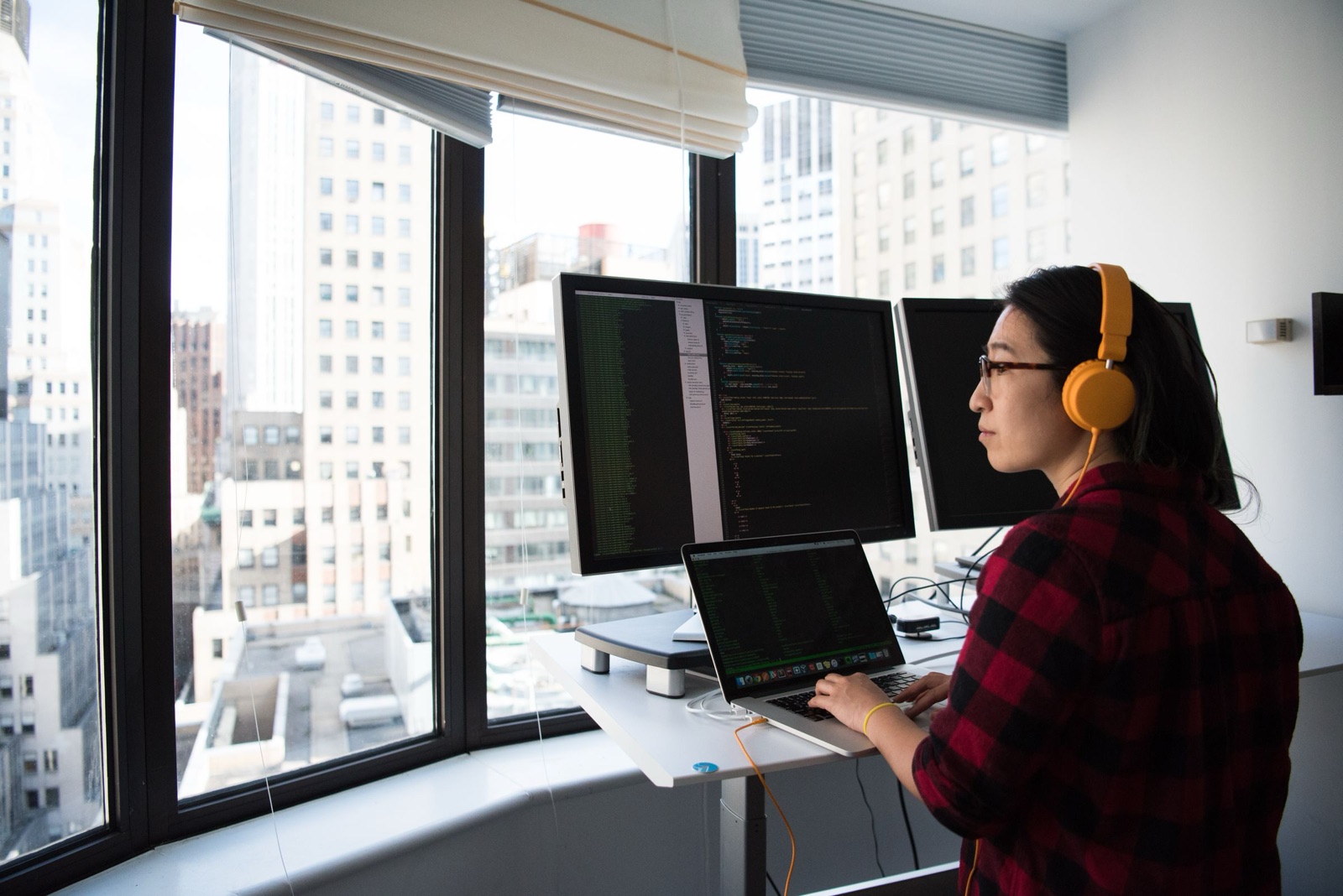 A developer at a standing desk with code across two monitors and city light behind